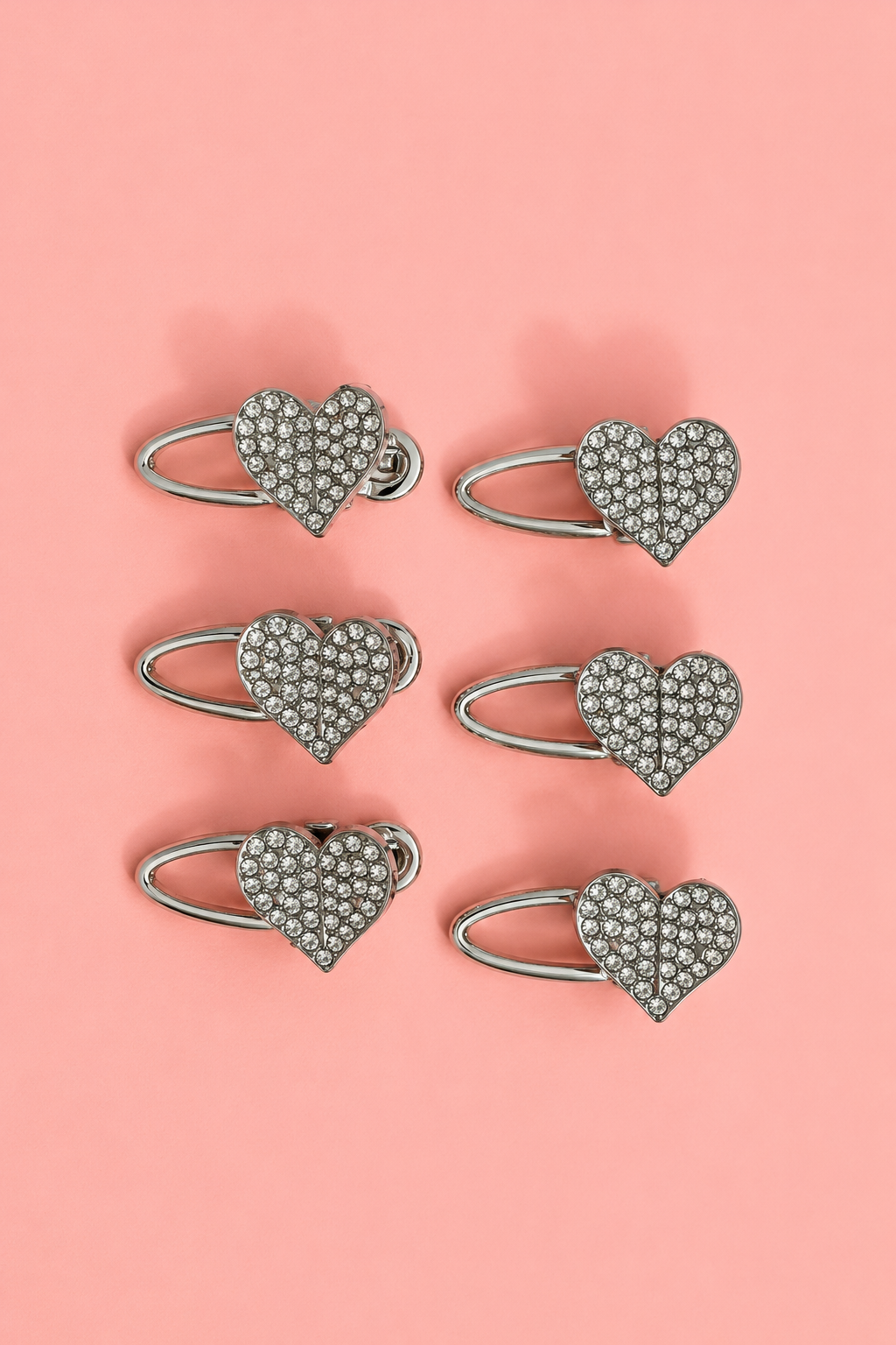 Set of six silver heart-shaped jewelry holders with rhinestones on a pink background
